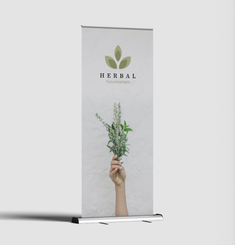 Referenzbild eines Messe-Roll-Ups für Herbal Naturkosmetik, das das Logo und eine Hand, die Kräuter hält, zeigt.